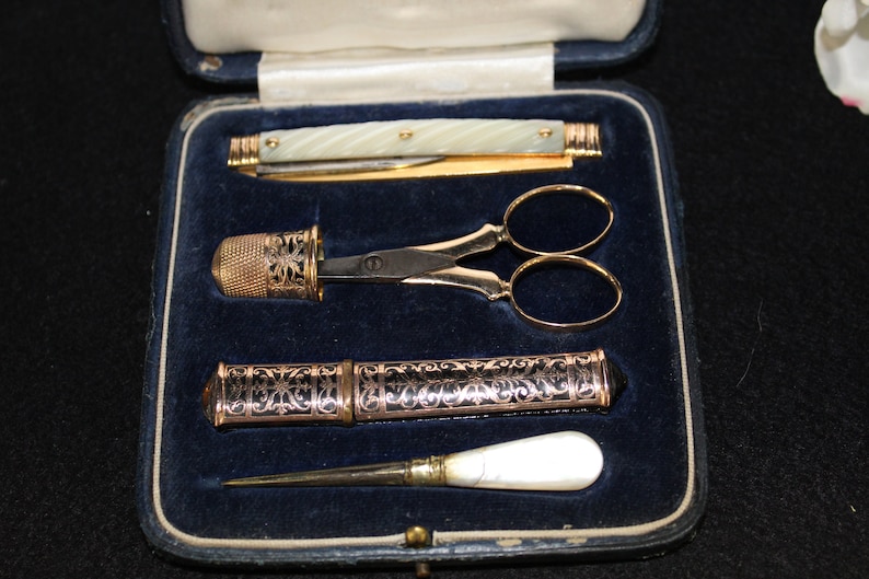 May include: A vintage sewing kit in a blue velvet box. The kit includes a pair of gold-plated scissors, a thimble, a needle case, and a small knife with a pearl handle.