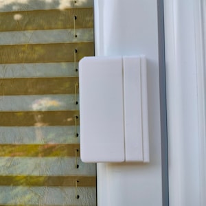 Może przedstawiać: Biały plastikowy zamek do okna z fakturowaną powierzchnią. Zamek jest przymocowany do białej ramy okna.