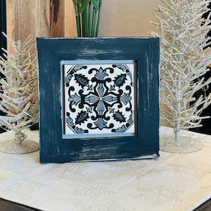 May include: A framed tile with a black and white geometric design. The frame is dark blue with white paint accents. The tile is set against a white background.