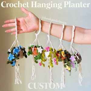 May include: Six crocheted hanging planters with different colored flowers and greenery. The planters are hanging from a person's arm. The text "@hookandclawco" and "CUSTOM" are visible in the image.