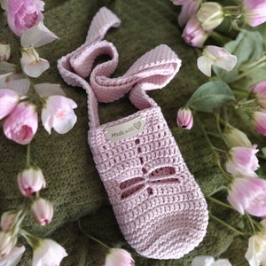 May include: A pink crocheted bag with a dragonfly design and a silver tag that says "Made with love".