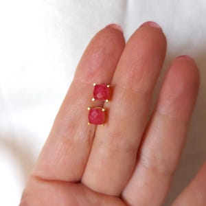 Op de afbeelding: Een paar gouden oorbel studs met rode vierkante edelstenen.