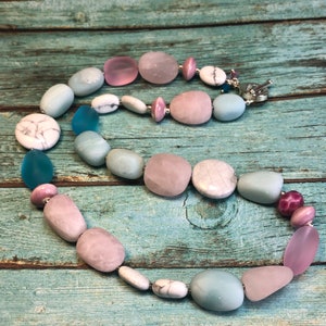 May include: A multi-coloured gemstone necklace featuring pink, blue and white stones. The necklace is made of smooth, rounded stones and is strung on a silver chain.