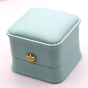 May include: A light blue square-shaped ring box with a gold latch.