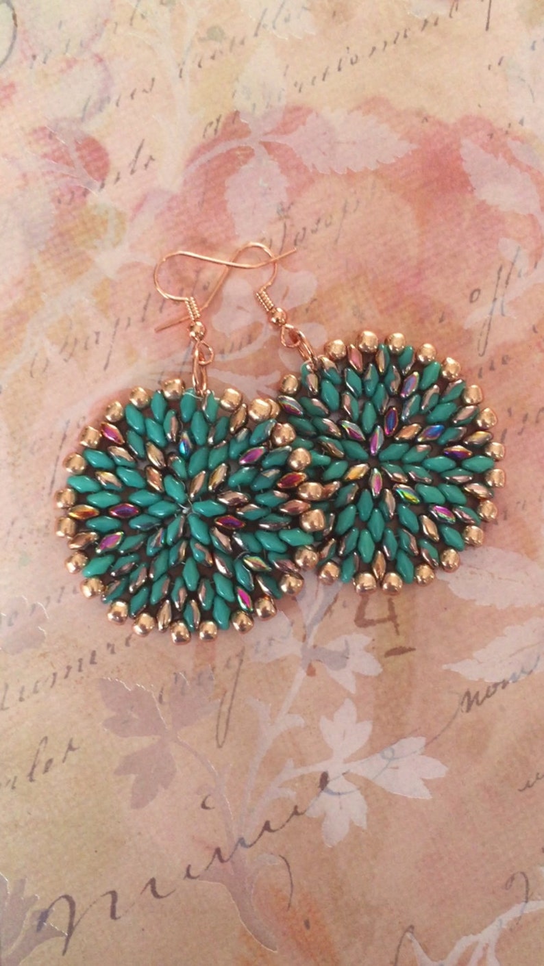 May include: A pair of round, turquoise and copper earrings with a beaded design. The earrings are made with small, iridescent beads and have a delicate, feminine look.