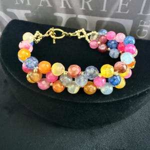 May include: A multi-colored beaded bracelet with a gold clasp. The bracelet features a variety of colors, including pink, blue, yellow, and orange.