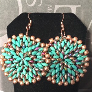 May include: A pair of turquoise and copper beaded earrings. The earrings are round and have a swirling pattern. The beads are iridescent and have a metallic sheen.