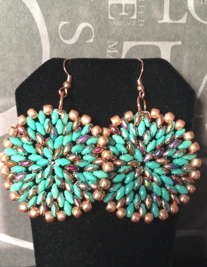 May include: A pair of turquoise and copper beaded earrings. The earrings are round and have a swirling pattern. The beads are iridescent and have a metallic sheen.