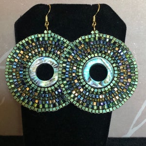 May include: A pair of large, round, green and gold beaded earrings with a iridescent center piece.