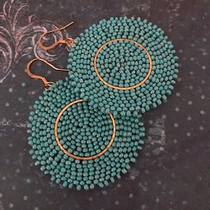 May include: A pair of turquoise blue beaded earrings with gold hoops. The earrings are round and have a circular design.