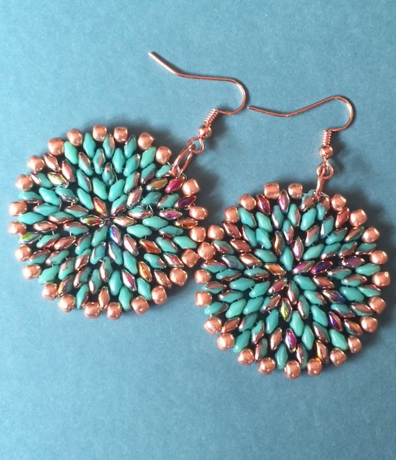 May include: A pair of copper and turquoise beaded earrings. The earrings are round and have a geometric design.