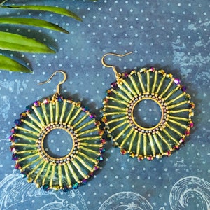 May include: A pair of large, round, gold earrings with a sunburst design. The earrings are made of iridescent glass beads and have a gold-toned metal hoop in the center.