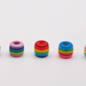 Puede incluir: Colección de cuentas de colores a rayas. Las cuentas son cilíndricas con un agujero en el centro. Los colores incluyen negro y blanco, rosa, morado, verde, rojo, azul y amarillo. Adecuado para la fabricación de joyas y manualidades.