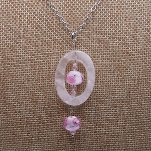 May include: A silver chain necklace with a clear oval pendant featuring two pink glass beads. The pendant has a delicate, openwork design.