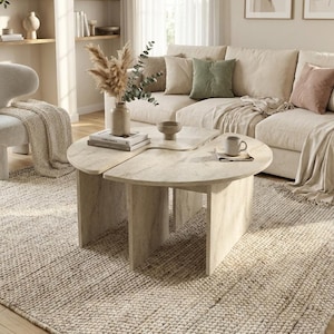 May include: A light beige, semi-circular coffee table with a smooth, stone-like finish and vertical panel legs. The table is composed of two separate pieces that fit together to form a larger surface, featuring a neutral, textured appearance.