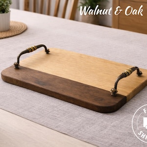 May include: A rectangular wooden tray with a light oak and dark walnut finish. It features curved metal handles with decorative accents. The tray is on a light gray surface. Text on the image reads "Walnut & Oak Tray".