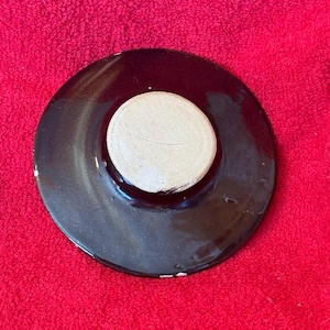 May include: A dark brown ceramic lid with a light beige, circular center. The lid is round with a slightly raised center. The surface has a glossy finish. The lid is likely for a pot or other kitchenware.
