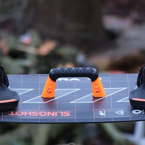 May include: Black and orange wakeboard with a black handle and the text "SLINGSHOT" printed on the board.