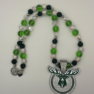 May include: A green and black beaded necklace with a silver pendant featuring a deer head with a green background and rhinestones.