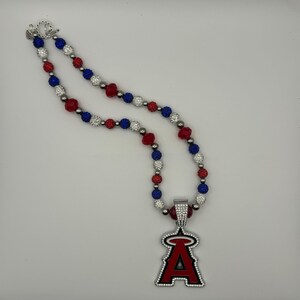 Puede incluir: Un collar de cuentas rojas, blancas y azules con un colgante plateado que presenta el logotipo del equipo de b&eacute;isbol de los &Aacute;ngeles de Los &Aacute;ngeles.