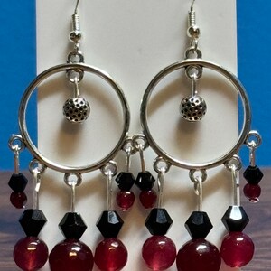 May include: Silver hoop earrings with dangling black and burgundy beads. The hoops have a textured ball charm hanging from them.