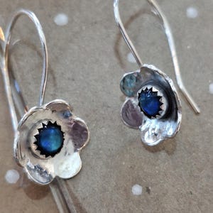 May include: A pair of silver earrings with a blue gemstone in the center of each flower-shaped design.