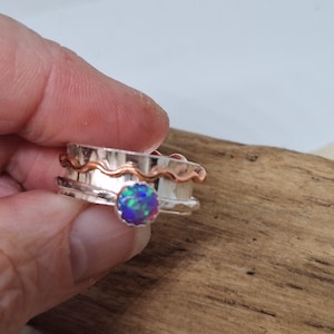 May include: A silver and copper ring with a wavy design and a round opal gemstone in the centre.