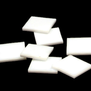 May include: A collection of small, white, square and rectangular tiles against a black background. The tiles are arranged in a scattered pattern, with varying orientations. The tiles appear to be made of a solid, opaque material.