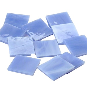May include: A collection of light blue square glass tiles. The tiles have a slightly translucent appearance, with subtle variations in color and texture. The tiles are arranged in a loose, overlapping pattern, suitable for mosaic projects or decorative applications.