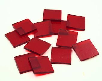 May include: A collection of red glass tiles, scattered on a white surface. The tiles are square and translucent, with a slight sheen.