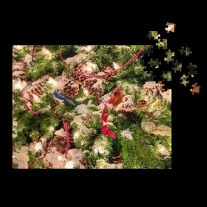 Puede incluir: Un rompecabezas con temática navideña que presenta un árbol de hoja perenne decorado. El árbol está adornado con piñas, guirnaldas rojas y pequeños adornos de pájaros. Las piezas del rompecabezas están dispersas alrededor de la imagen, lo que sugiere un estado incompleto.