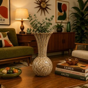 May include: A tall, beige and brown speckled ceramic vase with a bulbous base and a fluted, scalloped rim. The vase features a textured, mottled glaze finish and is filled with green eucalyptus branches, standing on a wooden coffee table.