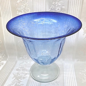 May include: A white ceramic mug with a black handle and the text "But First, Coffee" in a black, bold font. The mug is sitting on a white surface. The mug is approximately 4 inches tall.