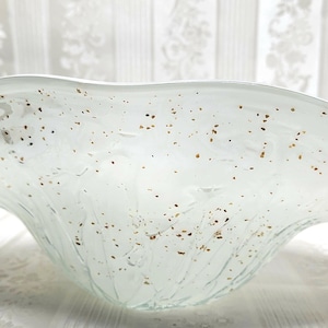May include: A decorative, clear glass bowl with a wide, undulating rim. The bowl has a speckled pattern of small, brown flecks throughout. The bowl is likely used for decorative purposes or serving.