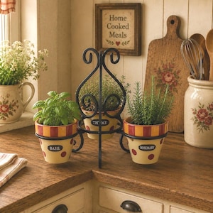 May include: A black metal tiered stand holding three ceramic pots labeled Basil, Thyme, and Rosemary. Each pot features a cream base with red polka dots and a red and yellow striped rim. The stand has a decorative scrollwork top handle.