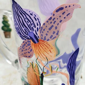 Puede incluir: Taza de vidrio transparente con un dise&ntilde;o floral colorido. El dise&ntilde;o presenta formas abstractas naranjas, moradas y azules que se asemejan a flores y hojas. La taza tiene un asa y est&aacute; decorada con un estilo caprichoso y art&iacute;stico.