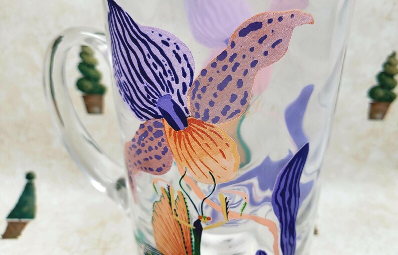 Puede incluir: Taza de vidrio transparente con un dise&ntilde;o floral colorido. El dise&ntilde;o presenta formas abstractas naranjas, moradas y azules que se asemejan a flores y hojas. La taza tiene un asa y est&aacute; decorada con un estilo caprichoso y art&iacute;stico.