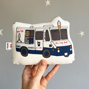May include: A white and blue ice cream truck pillow with the words "Milk Soft", "Sundaes", "Shakes", and "the very best" printed on it. The truck has a red and white striped ice cream cone on top.