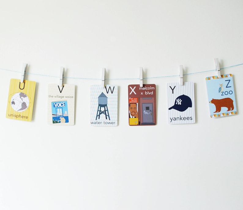 May include: A set of alphabet flashcards with illustrations and words. The flashcards are hung on a white wall with clothespins and a blue string.
