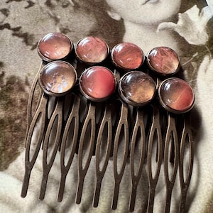 May include: A vintage-style hair comb with eight circular, iridescent cabochons in shades of pink, brown, and orange. The comb's tines are made of a dark, aged metal. The cabochons are set in a metal frame.