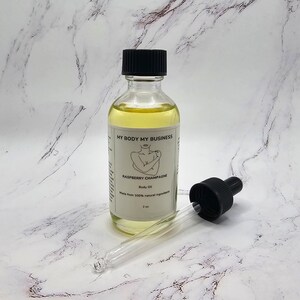 May include: A clear glass bottle with a black lid and a dropper. The bottle contains a yellow liquid and has a label that reads "My Body My Business Raspberry Champagne Body Oil Made from 100% natural ingredients 2 oz".