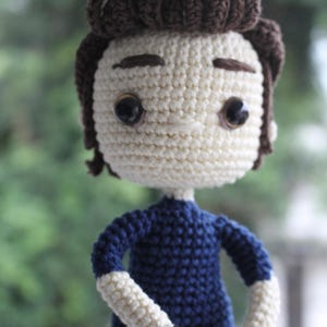 Puede incluir: Muñeca de ganchillo hecha a mano con cabeza color crema y peinado marrón oscuro. La muñeca viste una camisa azul marino con mangas blancas y pantalones negros. Tiene ojos negros grandes, un artículo único hecho a mano.