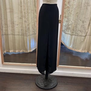 May include: A long black skirt with a slit in the front. The skirt is made of a smooth, flowing fabric.