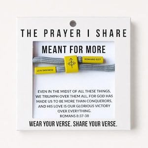 May include: A gray cord bracelet with yellow accents on a white display card. The card features the text THE PRAYER I SHARE MEANT FOR MORE, ROMANS 8:37-38, and WEAR YOUR VERSE. SHARE YOUR VERSE. The yellow components display a symbol and ROMANS 8:37.