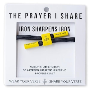 May include: A black rope bracelet with yellow accents. The bracelet features the text "IRON SHARPENS IRON" and "PROV. 27:17". The card reads "THE PRAYER I SHARE" and "WEAR YOUR VERSE SHARE YOUR VERSE".