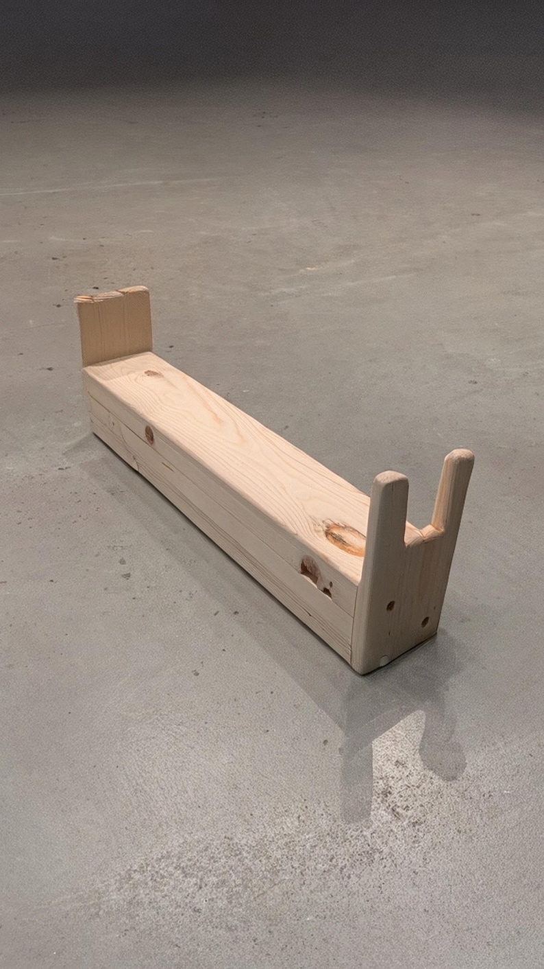 May include: A natural wood bench with a rectangular seat and two upright supports at each end. The bench is made of unfinished wood and has a simple, minimalist design. The bench is approximately 36 inches long.