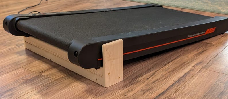 May include: A black treadmill with a red stripe and text on the side, resting on a light-colored wooden platform. The treadmill belt is black and the frame is black with red accents. The wooden platform is made of light-colored wood.