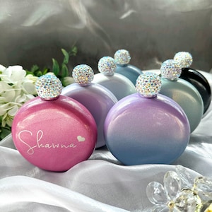 Könnte beinhalten: Fünf runde, metallische, Ombre-Kolben mit juwelenbesetzten Stopfen. Die Kolben sind in den Farben Rosa, Lila, Blau und Grau gehalten. Ein Kolben trägt den Namen "Shawna" auf sich.