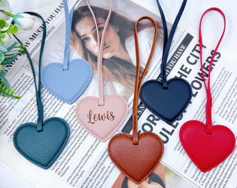 May include: A collection of heart-shaped leather tags in various colors: teal, light blue, pink with "Lewis" printed on it, brown, navy, and red. Each tag has a matching leather strap for hanging.