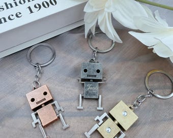 May include: Three robot-shaped keychains in bronze, silver, and gold tones. Each robot has a square head and body with rectangular arms and legs. The silver robot has the name "Jacob" engraved on its body. The keychains are on a silver ring.